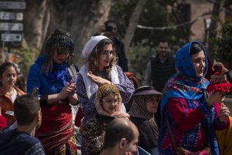 An Iranian woman wears traditional dresses and performs with a wooden goat doll, a symbol of the arrival of spring, in a ceremony to welcome the Iranian New Year outside the Cinema Museum in northern Tehran, Iran, on March 14, 2025. (Photo by Morteza Nikoubazl/NurPhoto via AP)