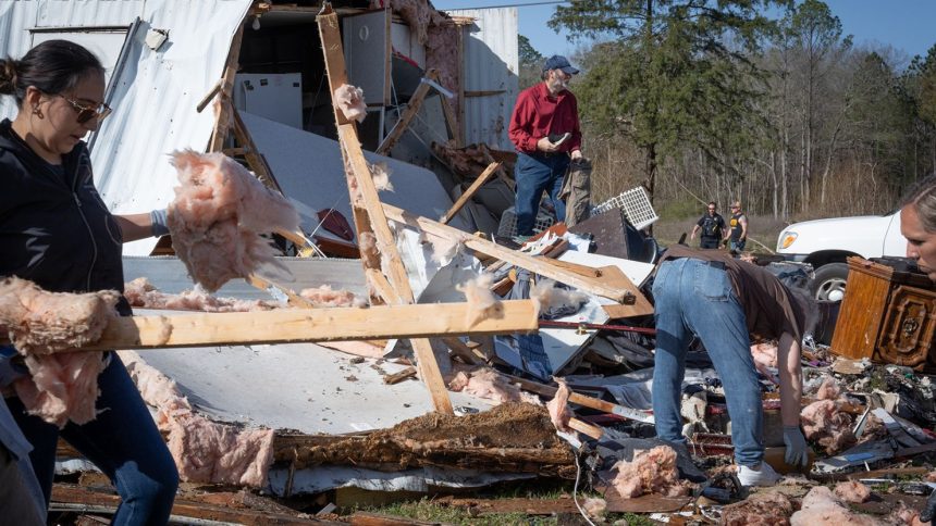 Tim Striegel, in red shirt (center), goes though his damaged belongings while volunteers help him clean up the morning after his mobile home was hit by a tornado on Sunday in Calera, Alabama.