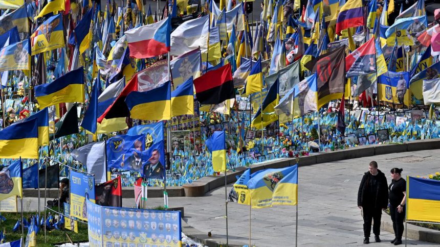 A couple walks by flags and portraits of fallen servicemen at a makeshift memorial for the fallen Ukrainian and foreign fighters, at the Independence Square in Kyiv, Ukraine, on Saturday.