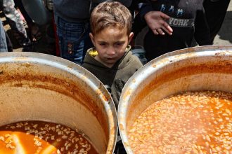 A Palestinian child waits to receive his portion of a hot meal, at a free food distribution point at the Nuseirat refugee camp in the central Gaza Strip on April 12.