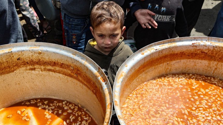 A Palestinian child waits to receive his portion of a hot meal, at a free food distribution point at the Nuseirat refugee camp in the central Gaza Strip on April 12.