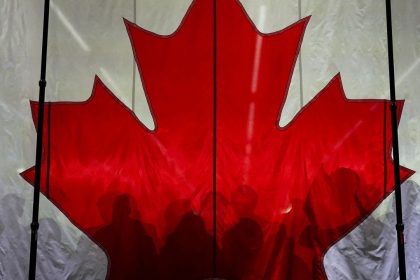 Supporters cast shadows on a Canadian flag as they gather prior to an election campaign event for Conservative Party of Canada's leader Pierre Poilievre, in Vaughan, Ontario, Canada April 22, 2025.