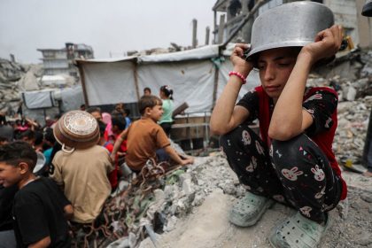 A girl puts a pot to her head as Palestinians wait to receive food cooked by a charity kitchen, in Beit Lahia, northern Gaza Strip, earlier this month.