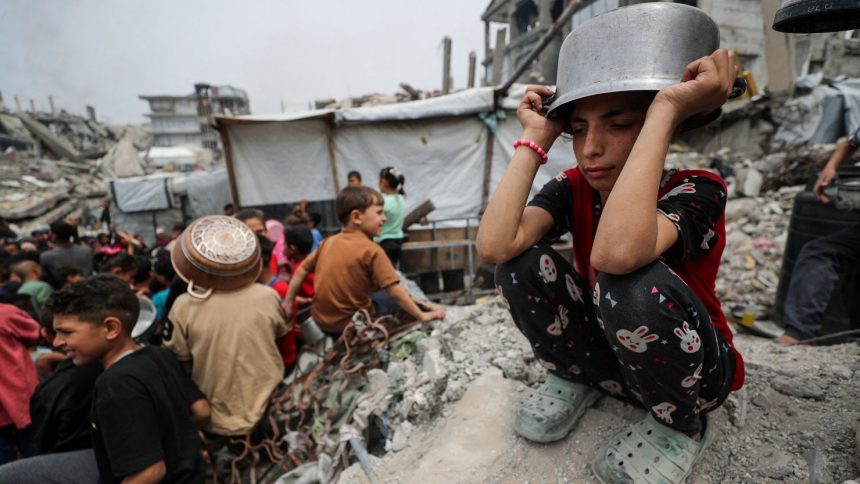 A girl puts a pot to her head as Palestinians wait to receive food cooked by a charity kitchen, in Beit Lahia, northern Gaza Strip, earlier this month.