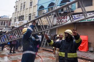 Firefighters carry a ladder outside of the building that caught fire in Hyderabad, India, on May 18, 2025.
