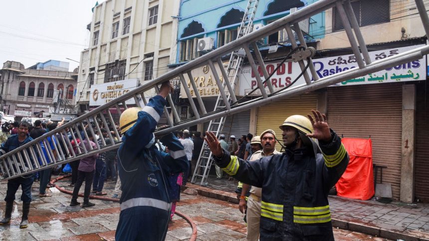 Firefighters carry a ladder outside of the building that caught fire in Hyderabad, India, on May 18, 2025.