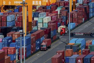 Trucks move amid containers stacked at a container terminal port on the Yangtze River in southwest China's Chongqing municipality.