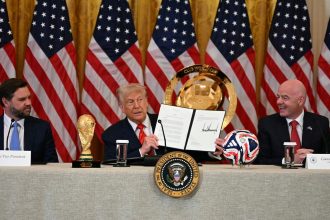 President Donald Trump holds up a document creating the "White House Task Force on the FIFA World Cup 2026" as US Vice President JD Vance, left, and FIFA president Gianni Infantino look on in the East Room of the White house in Washington, DC, on May 6.