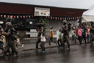 Members of the M23 armed group walk alongside residents through a street of the Keshero neighborhood in Goma, on Monday.