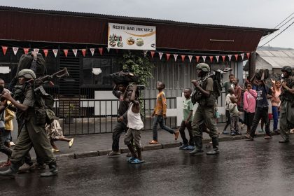 Members of the M23 armed group walk alongside residents through a street of the Keshero neighborhood in Goma, on Monday.