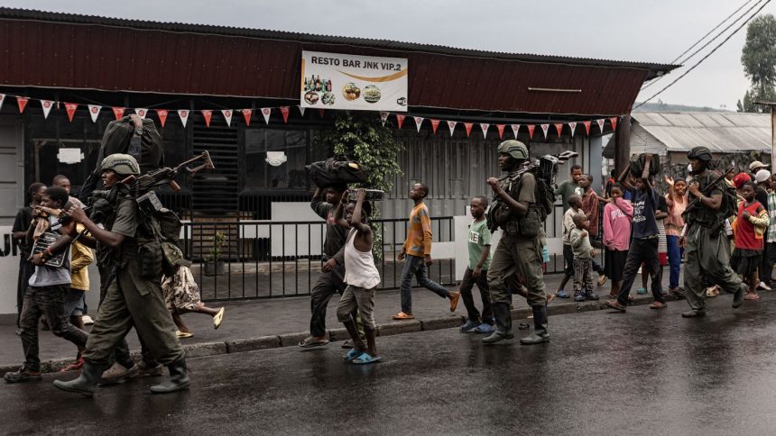 Members of the M23 armed group walk alongside residents through a street of the Keshero neighborhood in Goma, on Monday.