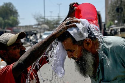 A volunteer pours water on a pedestrian's head to cool off during a hot summer day along a street in Karachi on April 5, 2025.