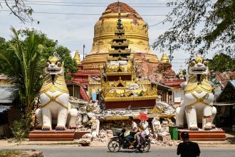 This photo taken on April 12, 2025 shows people driving past the debris of a damaged Buddha statue in Inwa on the outskirts of Mandalay, following the devastating March 28 earthquake.