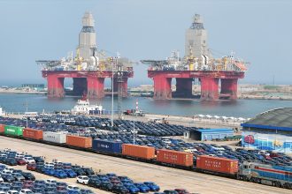 A view of new cars and two offshore drilling platforms waiting for shipment in a port in Yantai in east China's Shandong province on May 7, 2025.