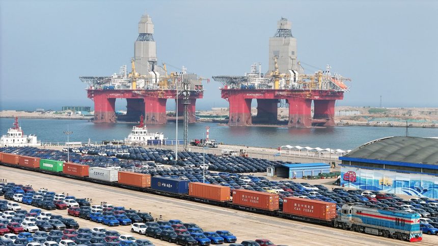 A view of new cars and two offshore drilling platforms waiting for shipment in a port in Yantai in east China's Shandong province on May 7, 2025.
