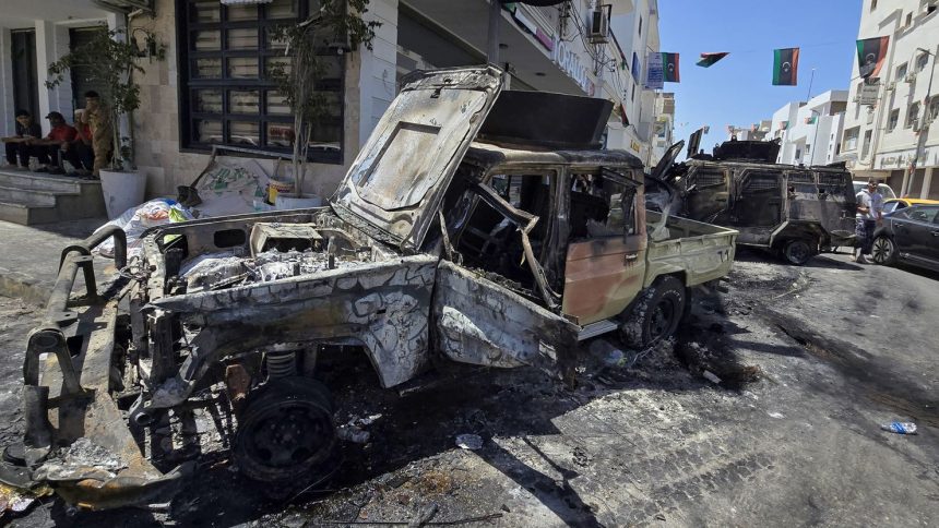 People sit at a coffee shop next to cars destroyed during overnight clashes in the southern district of Abu Salim in the Libyan capital Tripoli on May 13, 2025.