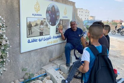 Ali Samoudi next to a photo of slain American-Palestinian journalist Shireen Abu Akleh, outside the entrance of Jenin Camp, in Jenin, West Bank in 2022