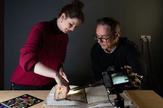 Conservator Sally Kilby and Błażej Mikuła photograph inside the folds of a medieval manuscript that was used as the cover for another book later on.