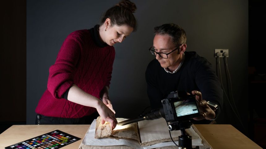 Conservator Sally Kilby and Błażej Mikuła photograph inside the folds of a medieval manuscript that was used as the cover for another book later on.