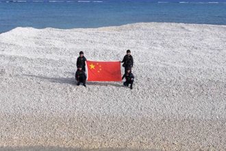 Chinese coast guard offices display their national flag on a tiny sandbar in the disputed Sandy Cay in April, 2025.