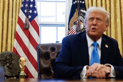 The 2026 men's FIFA World Cup trophy is visible behind US President Donald Trump as he speaks with reporters before signing two executive orders in the Oval Office of the White House on February 4.