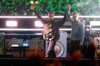 Liam Gallagher, left, holds the hand aloft of Noel Gallagher from the band Oasis as they perform during their reunion concert on Friday, July 4, 2025, in Cardiff.